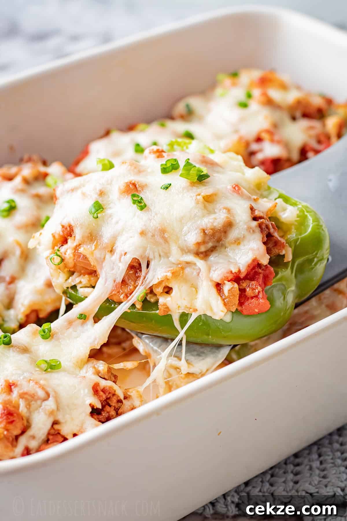 Baked ground beef stuffed pepper with melted cheese over white pan.