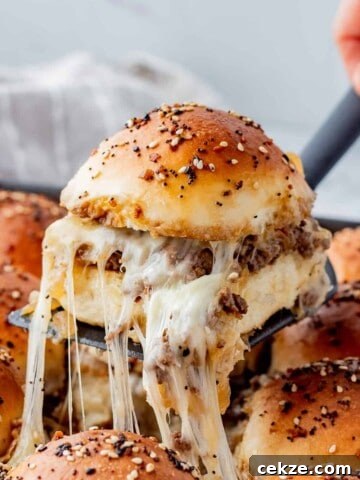 Dinner roll sliced in half with ground beef and caramelized onion filling with cheese on a black spatula.