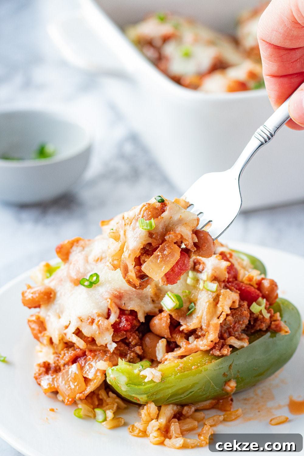 Cooked ground beef stuffed pepper with cheese on top with fork on a white plate.