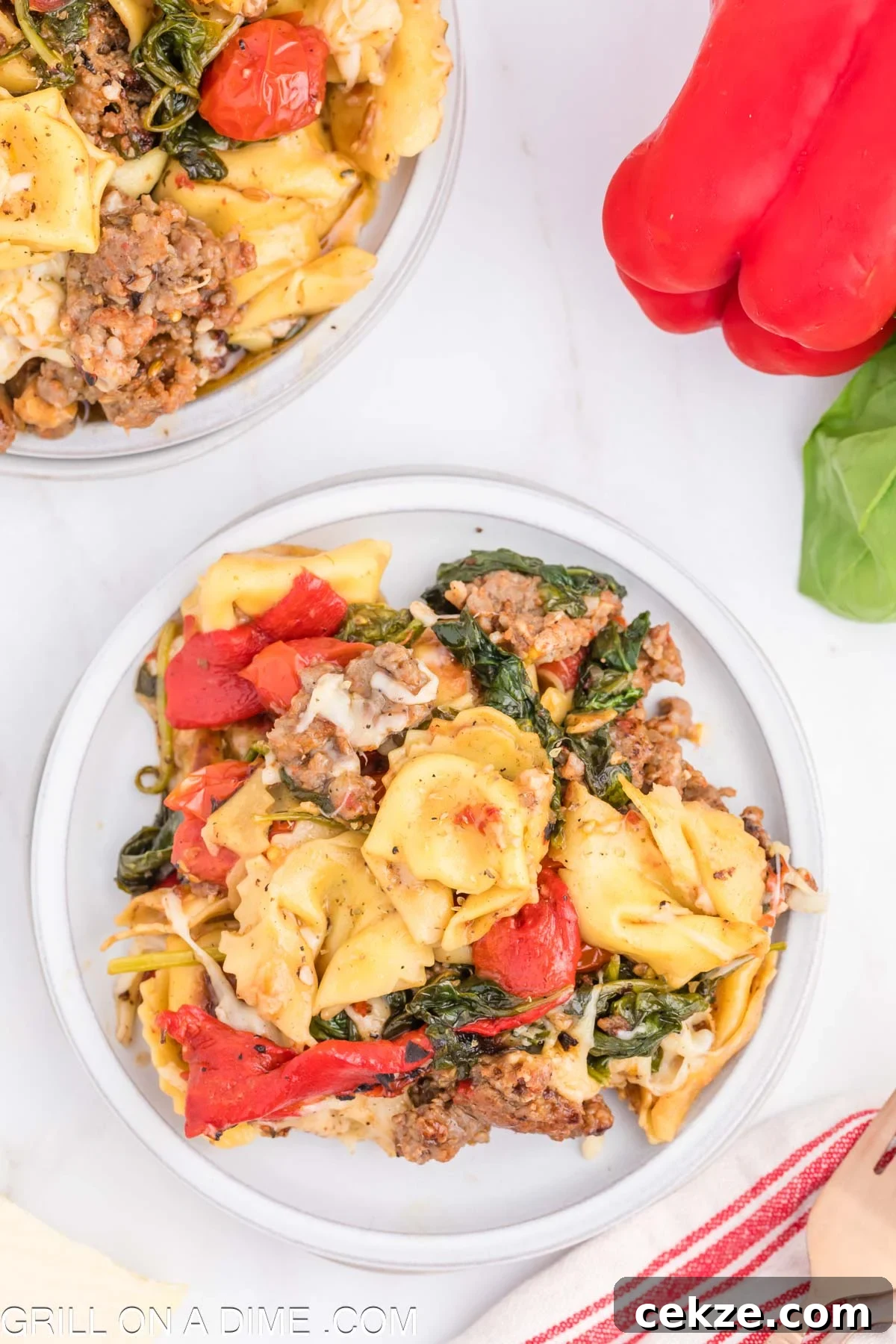 Cooked Tortellini and Sausage on a plate mixed with tomatoes and cooked spinach