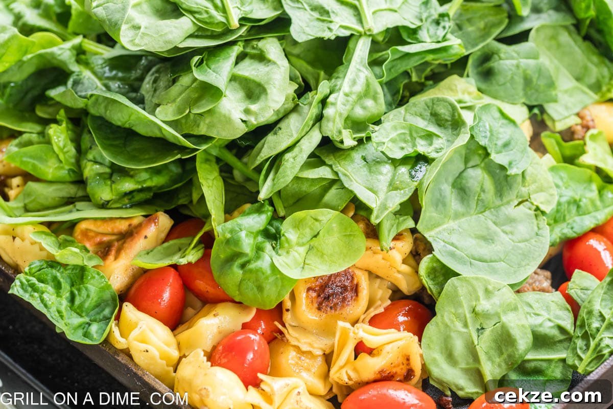 Topping the tortellini and cherry tomatoes with the fresh spinach on the griddle