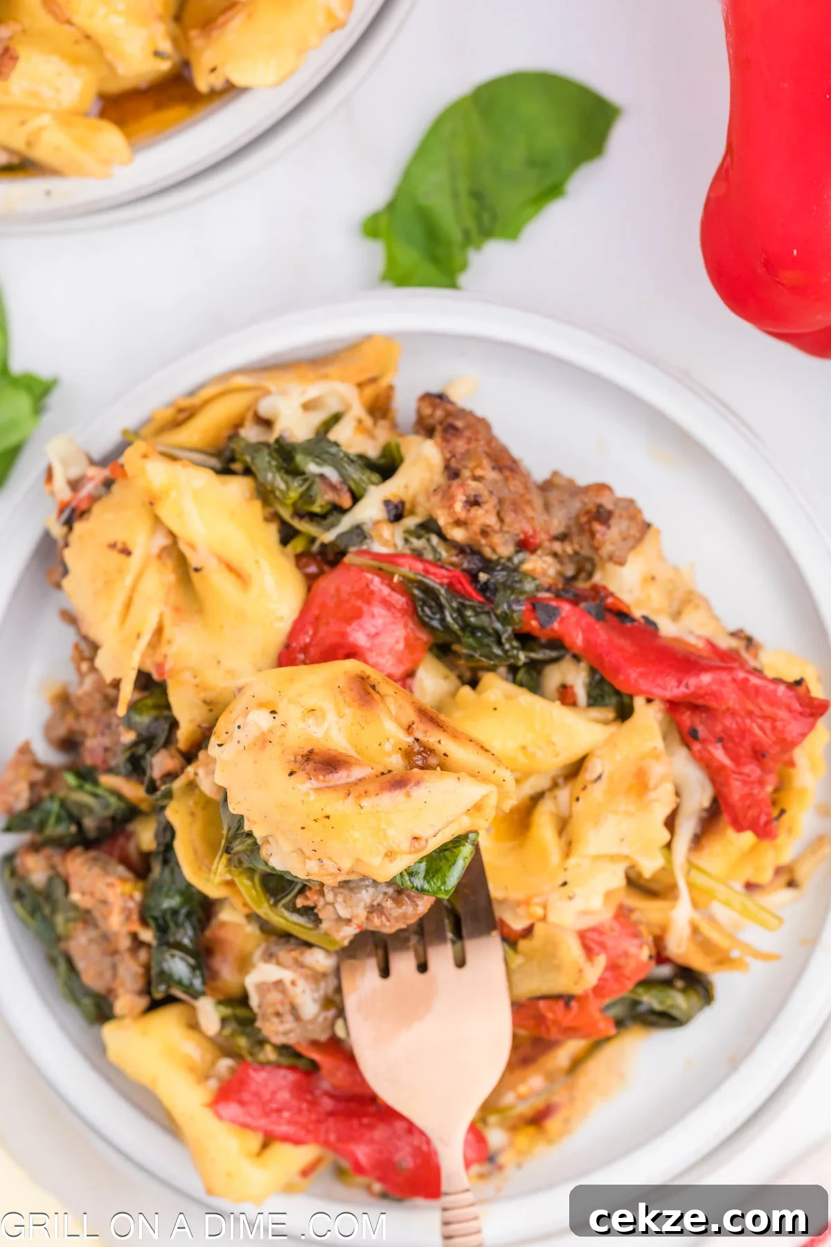 Cooked Tortellini and Sausage, tomatoes, and spinach on a plate with a fork