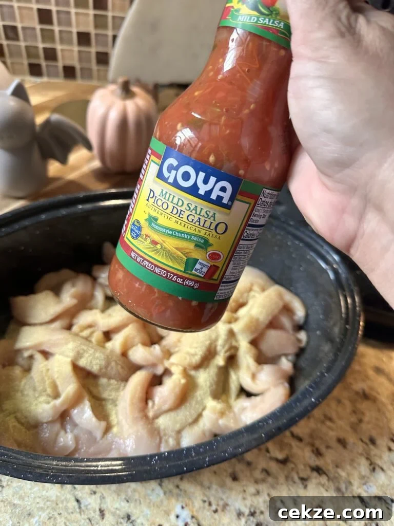 A bottle of Goya Pico De Gallo held in front of shredded raw chicken in a cooking dish