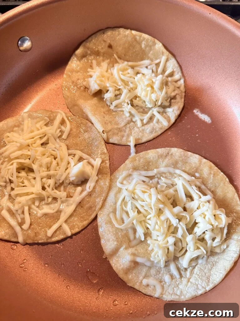 Shredded cheese on three small tortillas cooking in a pan
