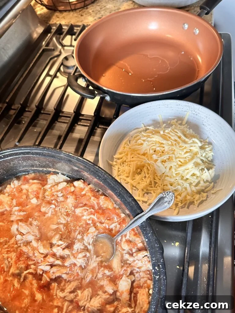 Shredded chicken in red sauce next to a bowl of shredded cheese and a pan with oil in it