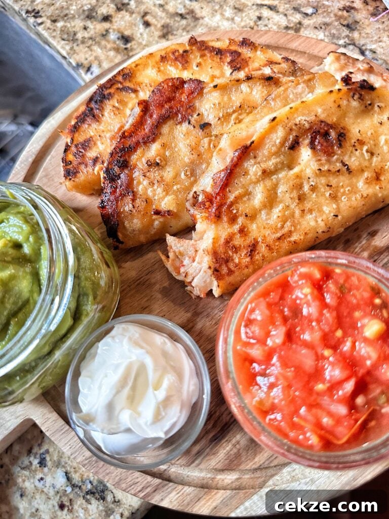 A close up of the finished crispy chicken tacos next to glass containers of guacamole, sour cream, and salsa