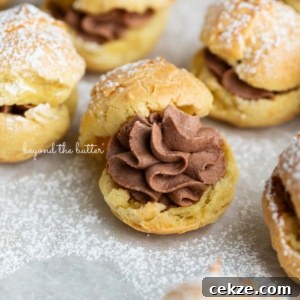 How to Make Classic Cream Puffs: Light Choux Pastry Recipe 13 Cream puffs filled with chocolate whipped cream and dusted with powdered sugar on a parchment paper lined baking sheet.