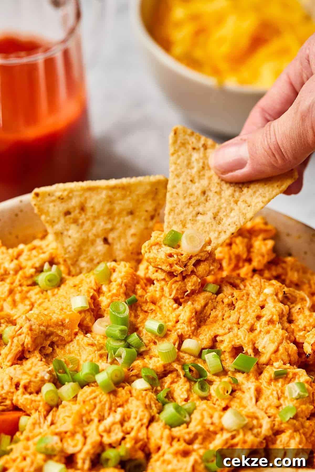 a hand dipping a tortilla chip into buffalo dip