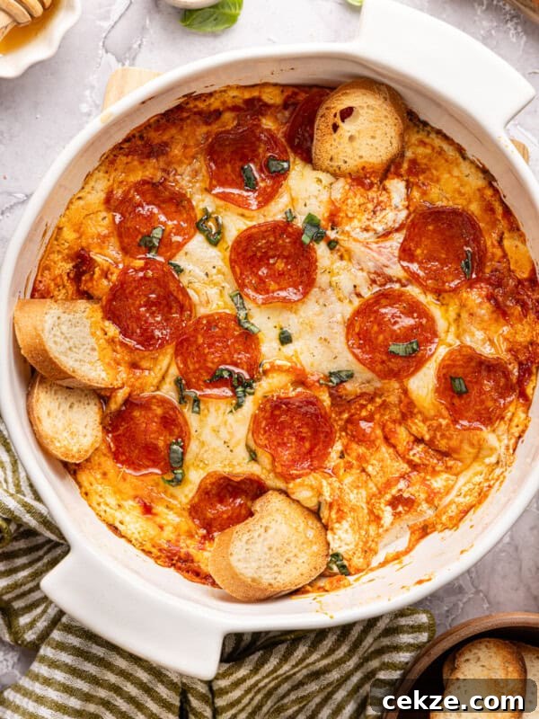 pizza dip in a casserole dish topped with pepperonis and basil with bagette slices stuck into it
