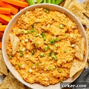 buffalo chicken dip in a white bowl with chips dipping in surrounded by chips and veggies.