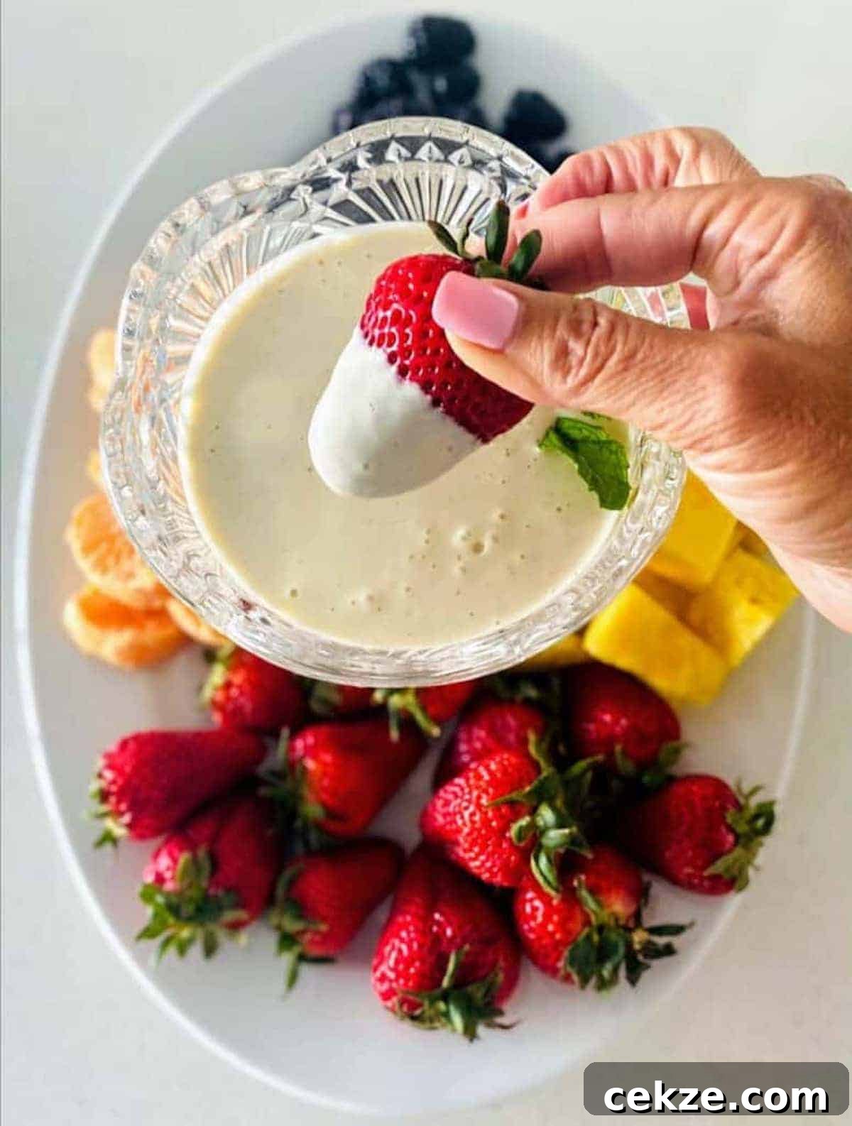 I am dipping a strawberry into the easy vegan fruit dip recipe.