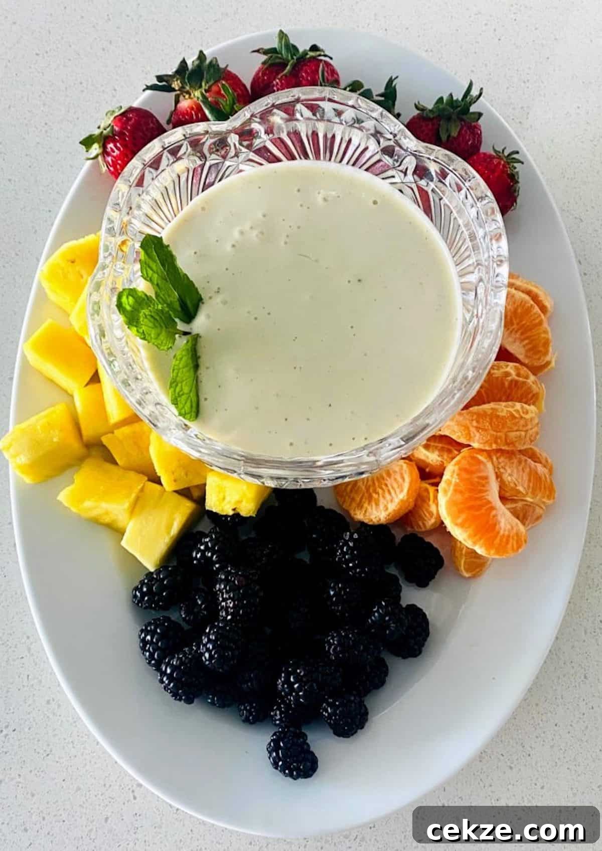 Fruit dip in a bowl centered on a tray with pineapple, strawberries, blackberries, and mandarin oranges.