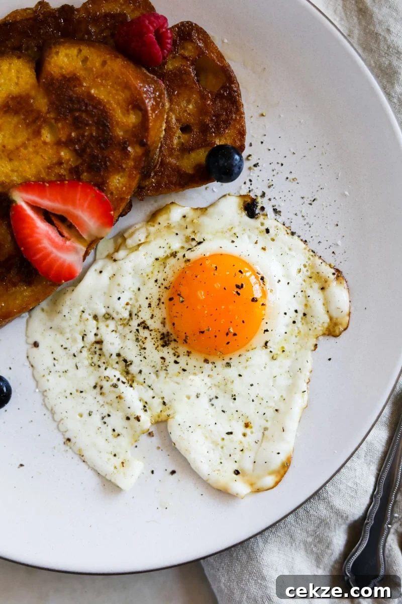 Perfect Sunny-Side-Up Eggs: Step-by-Step Cooking Guide 2 Sunny side egg with salt and pepper on a plate with sourdough French toast and berries.