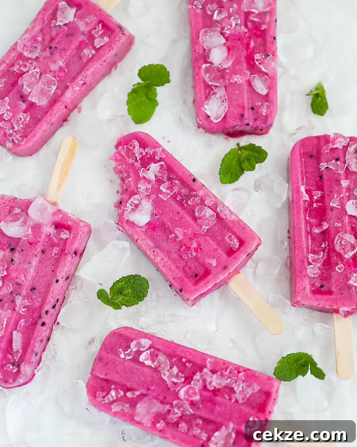 Refreshing Dragon Fruit Popsicle Recipe for Summer Treats 2 6 bright pink popsicles on a white marble board. Garnished with fresh mint and ice