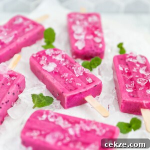 Refreshing Dragon Fruit Popsicle Recipe for Summer Treats 14 6 popsicles on a white marble slab. The pops and board are garnished with sprigs of fresh green mint and crushed ice.
