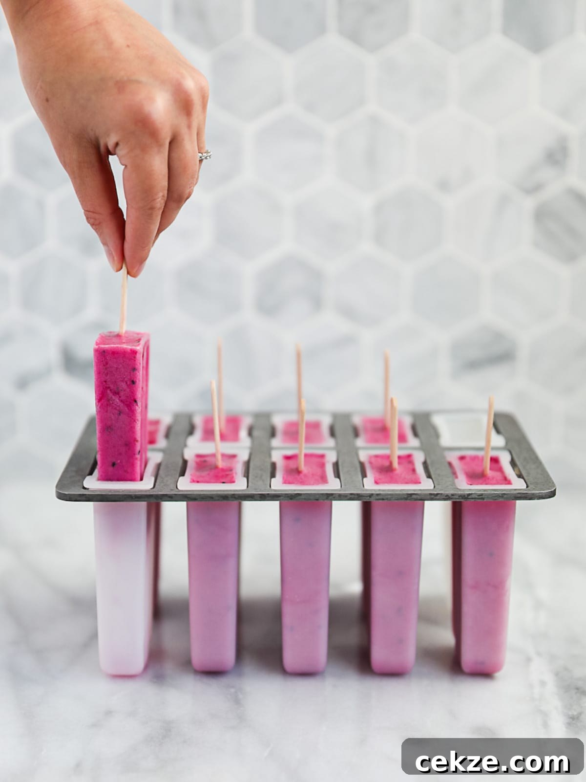 Refreshing Dragon Fruit Popsicle Recipe for Summer Treats 6 A hand pulling a bright pink popsicle from a popsicle mold.