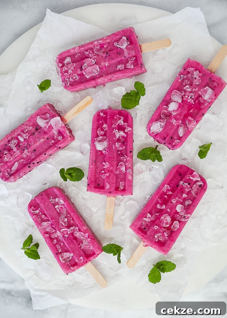 Refreshing Dragon Fruit Popsicle Recipe for Summer Treats 7 An overhead shot of bright pink popsicles on a white board and white parchment paper.