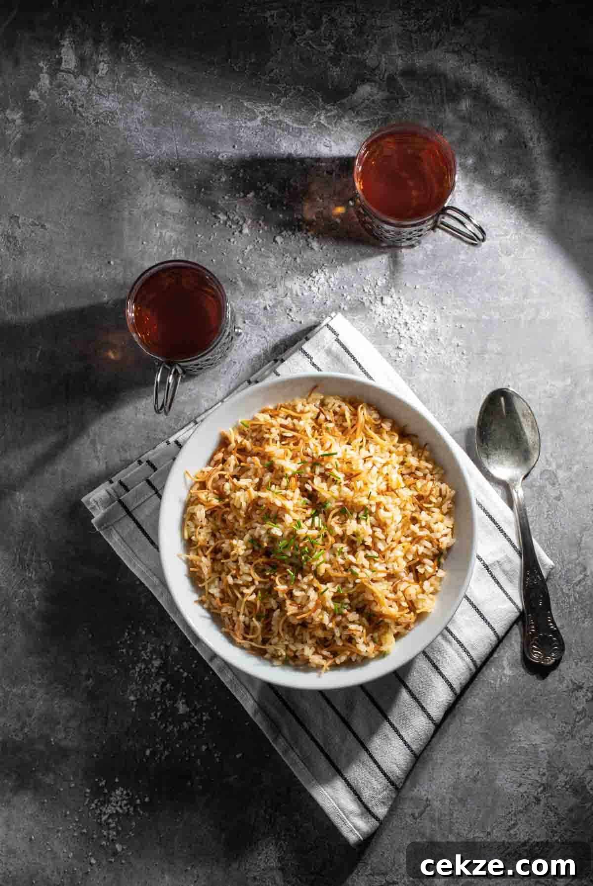 Authentic Egyptian Rice with Toasted Vermicelli Recipe 2 Egyptian rice in a white bowl with two cups of tea in glass mugs.