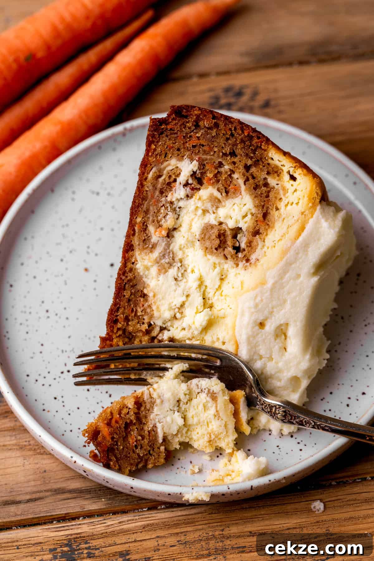 Carrot Cake Cheesecake Recipe: Moist Layered Dessert with Cream Cheese Frosting 11 Slice of cheesecake on a plate with a fork inserted.