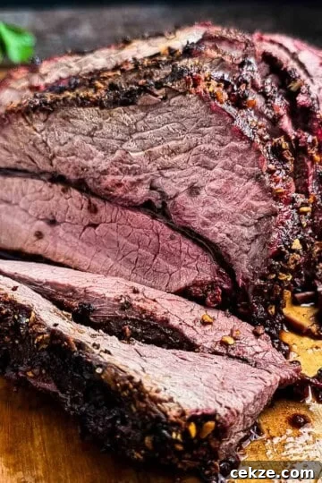 Slicing a juicy medium-rare smoked venison roast on a wooden cutting board.