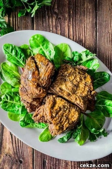 Venison pot roast on a bed of spinach leaves on a white platter.