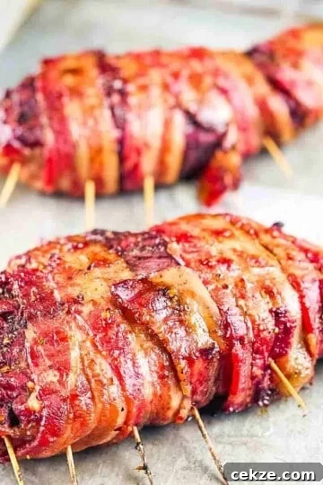 Two smoked bacon wrapped venison backstraps on a baking sheet.