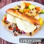 A venison Philly cheesesteak sandwich on a white plate with a side salad.