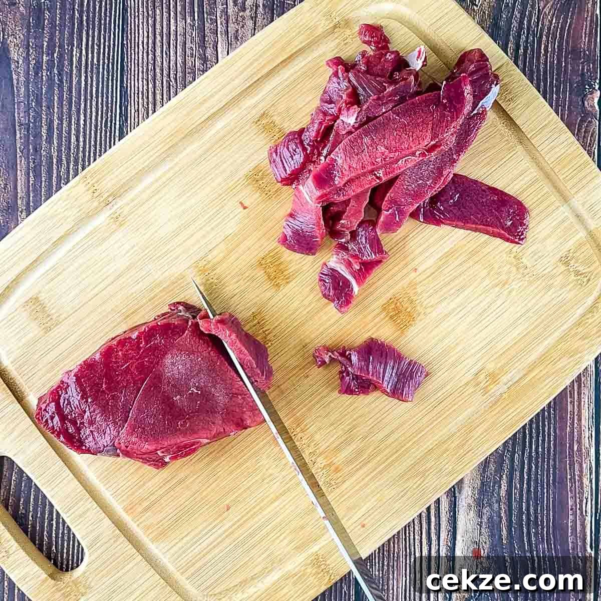 A knife cutting the venison into thin strips on a cutting board.