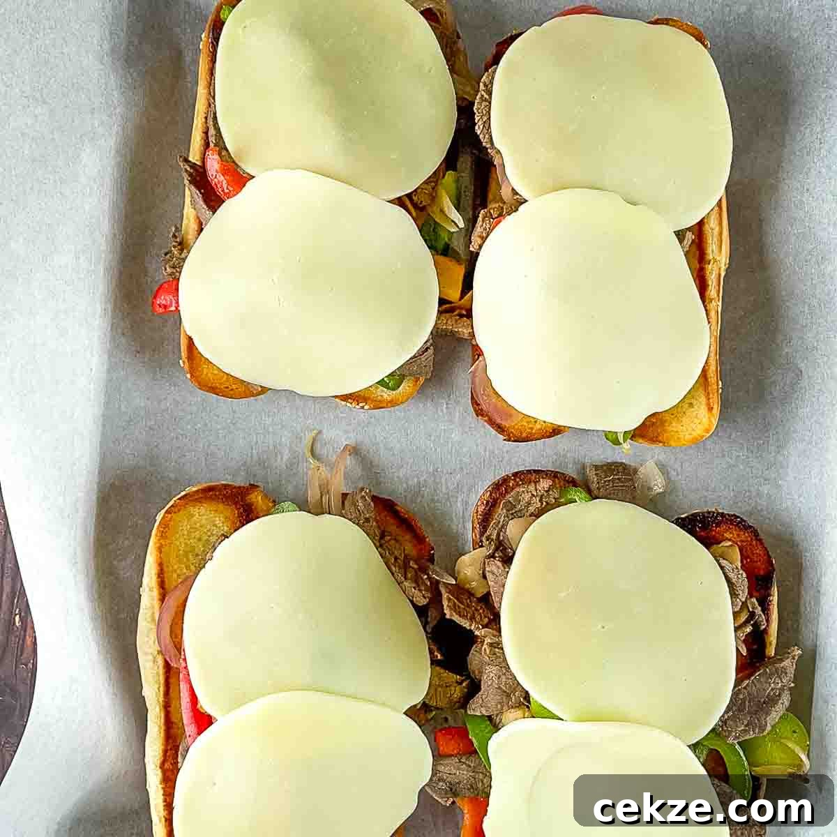 The toasted hoagie buns topped with cooked venison, vegetables, and slices of provolone cheese.