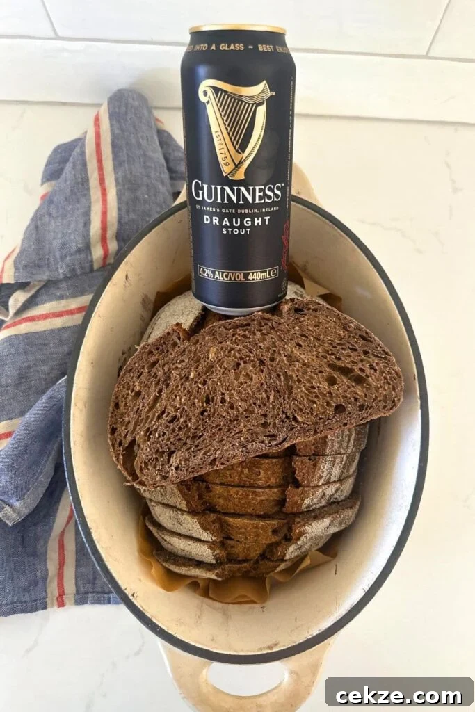Sourdough Guinness Beer Bread — St. Patrick's Day Loaf 3 A loaf of sourdough bread that has been made with Guinness. The dark loaf of sourdough is sitting in a cream enamel Dutch Oven and there is a can of Guinness sitting on the edge of the Dutch Oven.