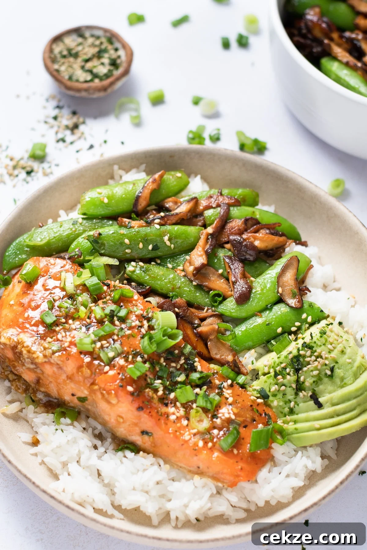 Plate with rice, miso butter salmon, sauteed shiitake mushrooms and snap peas, sliced avocado, green onions and furikake seasoning