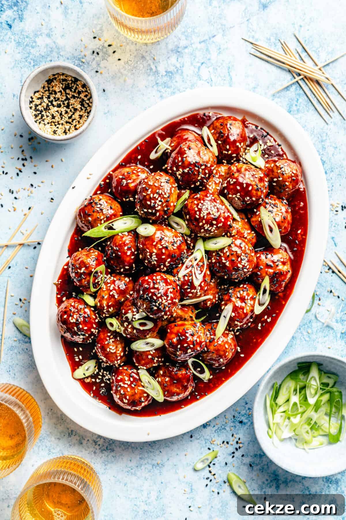 Korean BBQ Chicken Meatballs with Gochujang Glaze 2 Korean-Inspired BBQ Chicken Meatballs on white oval platter with beer in corner plus other garnishes.