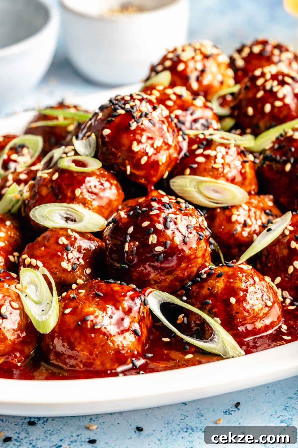 Korean BBQ Chicken Meatballs with Gochujang Glaze 3 Close up of Korean-Inspired BBQ Chicken Meatballs on white platter. Meatballs garnished with sesame seeds and green onions.