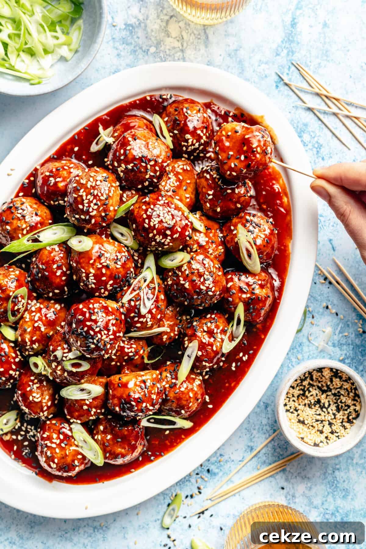 Korean BBQ Chicken Meatballs with Gochujang Glaze 5 Platter of Korean-Inspired BBQ Chicken Meatballs with hand holding toothpick reaching in.