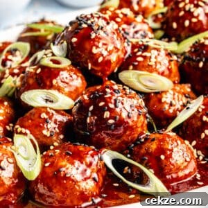 Close up of Korean-Inspired BBQ Chicken Meatballs on white platter. Meatballs garnished with sesame seeds and green onions.
