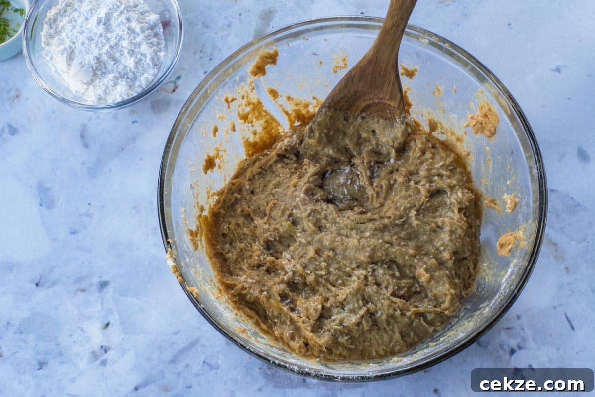 Tropical Banana Bread with Lime Glaze Recipe 9 Coconut being stirred into batter with a wooden spoon, in a large glass bowl.