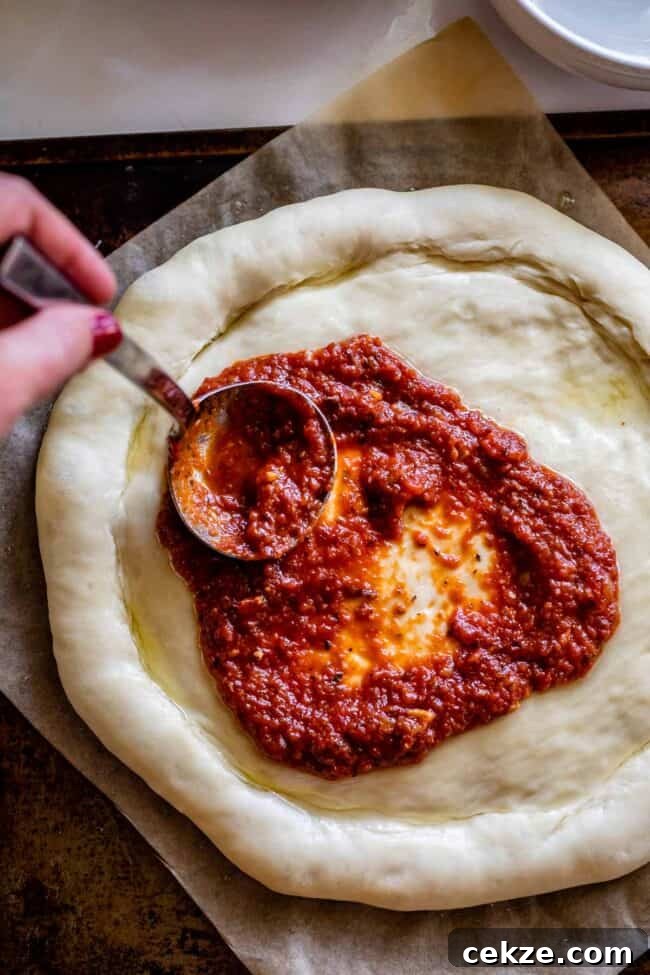 Classic Homemade Pizza Sauce Recipe for Perfect Pies 3 pizza sauce recipe being spread on a pizza dough with a ladle.