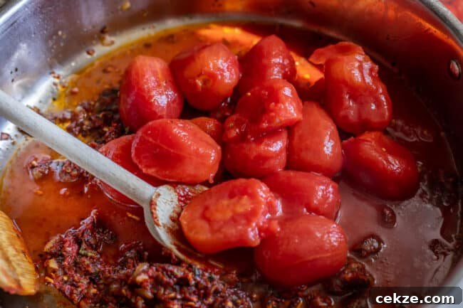 Classic Homemade Pizza Sauce Recipe for Perfect Pies 5 whole canned tomatoes being added to a pan to make best pizza sauce.