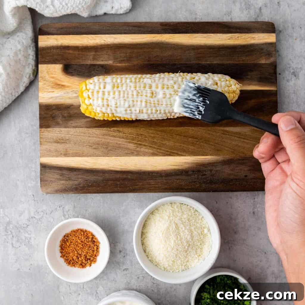 Authentic Elotes Recipe: Mexican Street Corn with Cotija & Lime 4 brushing mayonnaise on corn cob