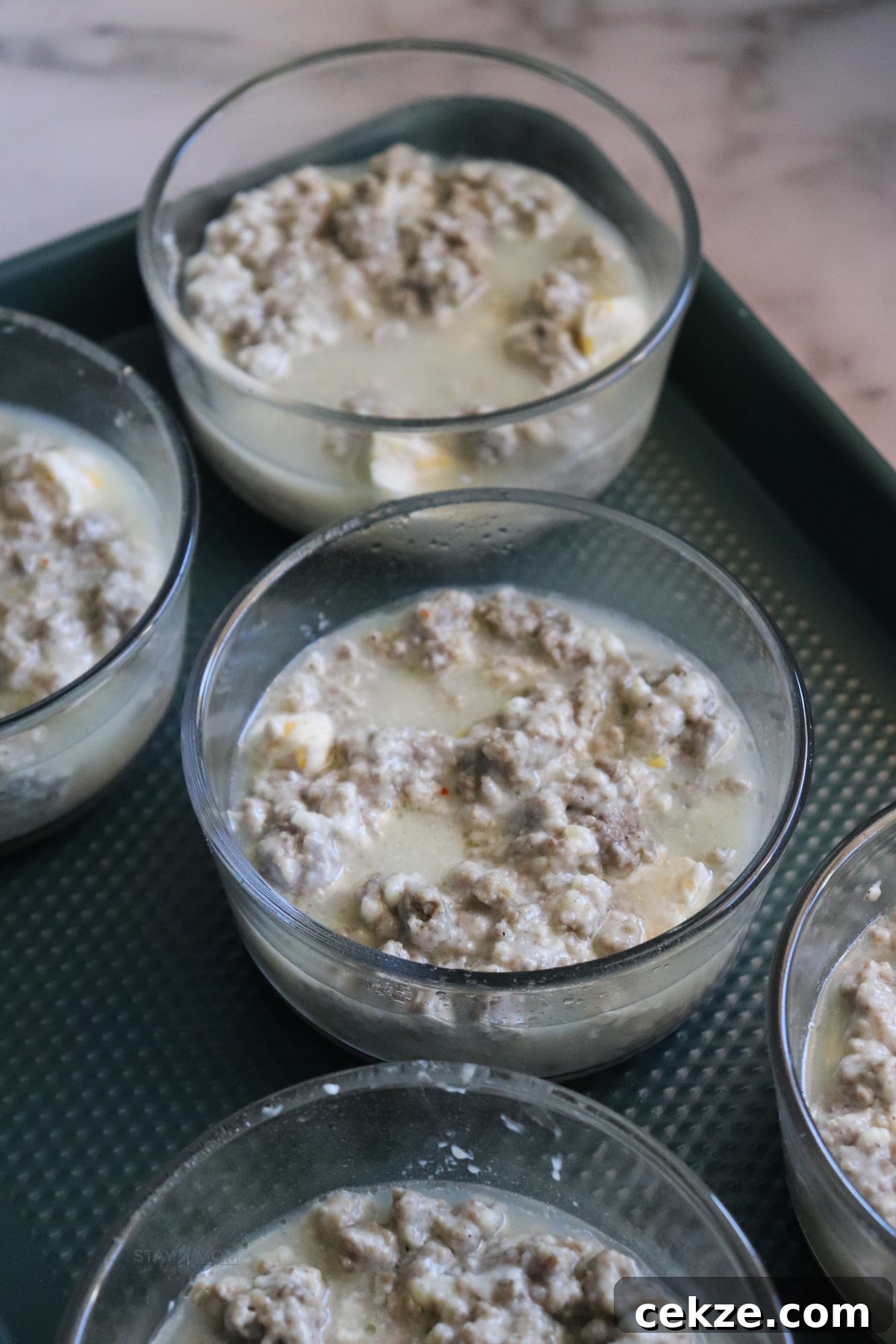 Biscuits and gravy casseroles showing oven safe containers filled with biscuits cut up and topped with egg whites and sausage gravy.