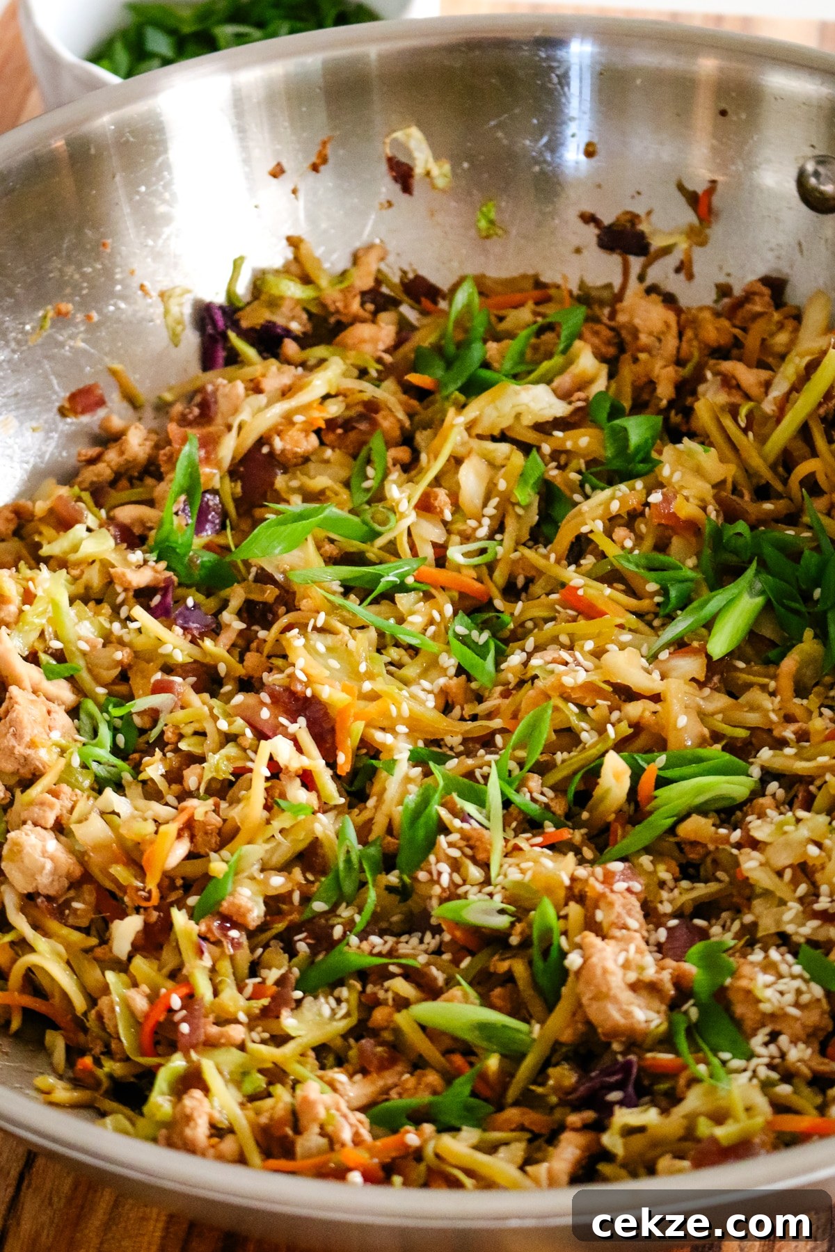 Keto Egg Roll in a Bowl Recipe: Quick Low-Carb Stir-Fry 7 egg roll in a bowl in a large wok with green onions garnished on top.