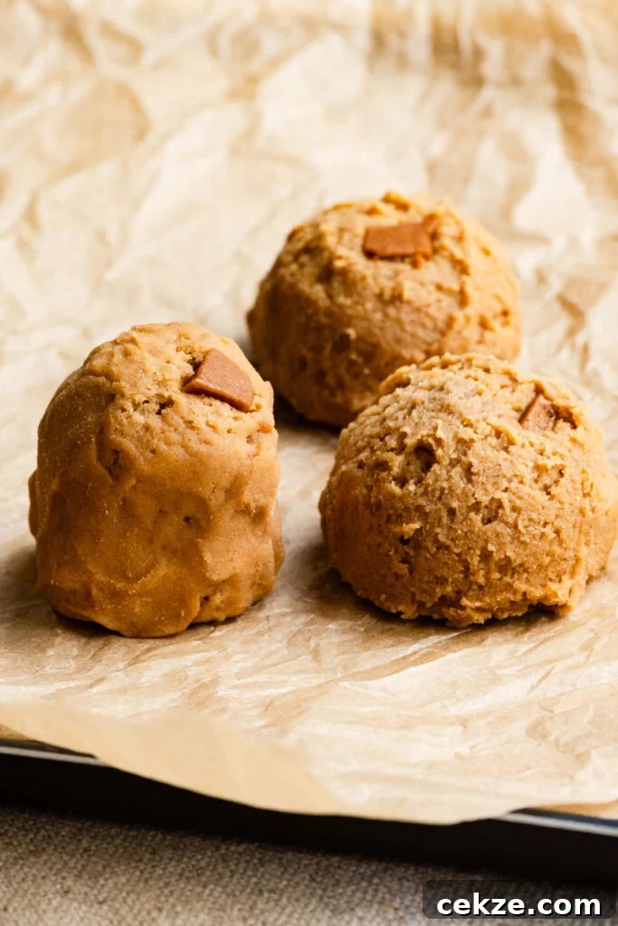Brown Sugar Toffee Cookies Recipe — Chewy Caramelized Treats 5 A tall cookie dough mound next to round cookie dough scoops on parchment paper.