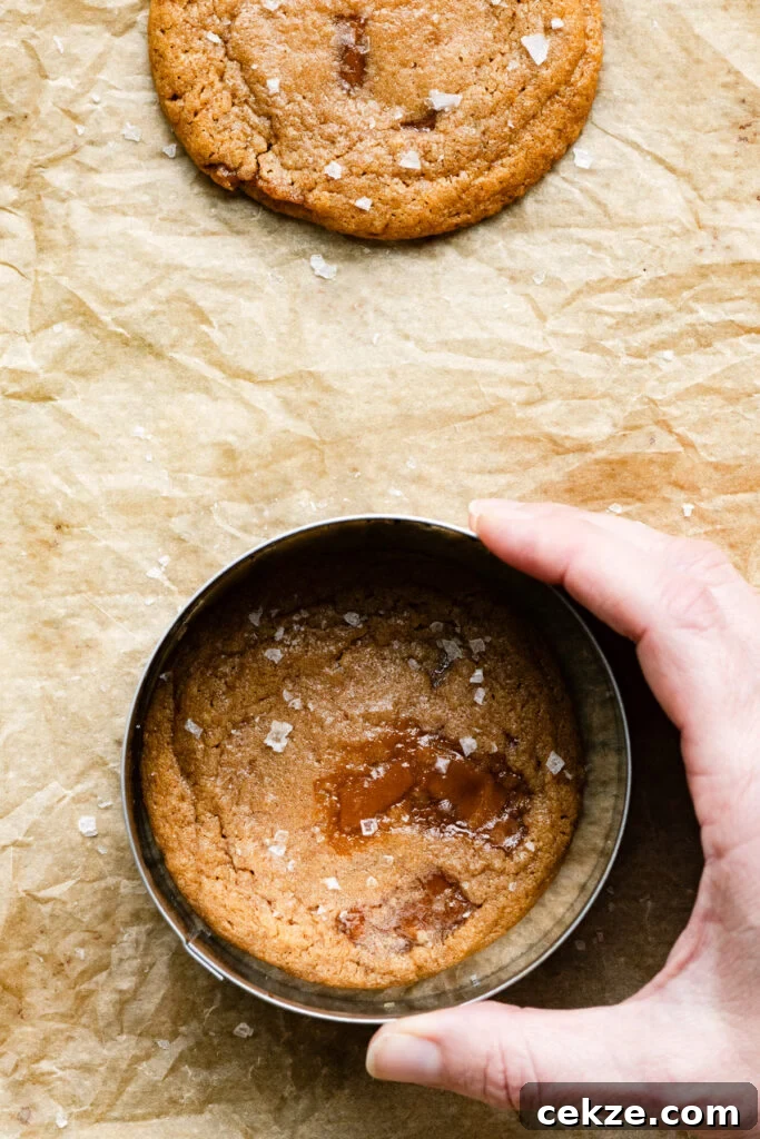 Brown Sugar Toffee Cookies Recipe — Chewy Caramelized Treats 7 A hand reshaping a cookie with a metal ring on a baking tray.