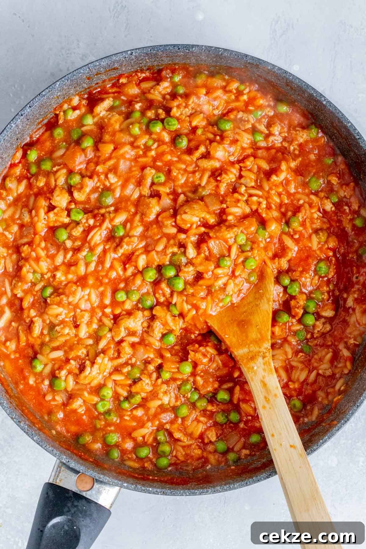 One-Pot Turkey and Pea Orzo Skillet Recipe 7 Overhead view of one pot orzo with turkey and peas being stirred in the skillet.