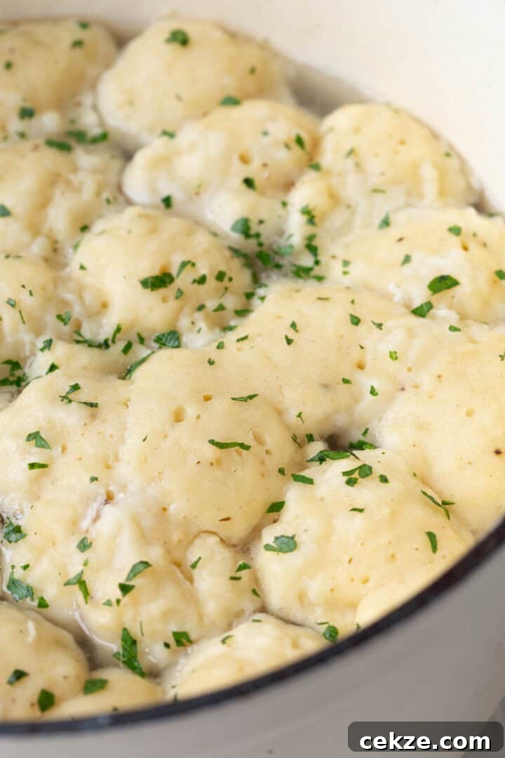 fluffy dumplings in a large pot, topped with chopped parsley.