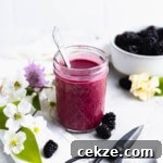 Jar of blackberry curd with a silver spoon sticking out of the top. Berries, flowers and a pair of floral scissors are laid out around it.