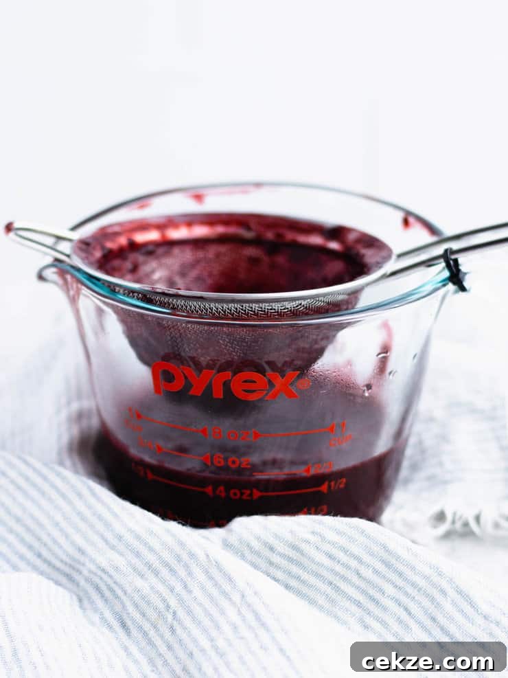 Small mesh sieve over a glass pyres measuring cup with pureed blackberry being worked through it.
