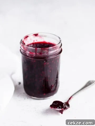 jar of blackberry cherry jam with a spoon of jam next to it