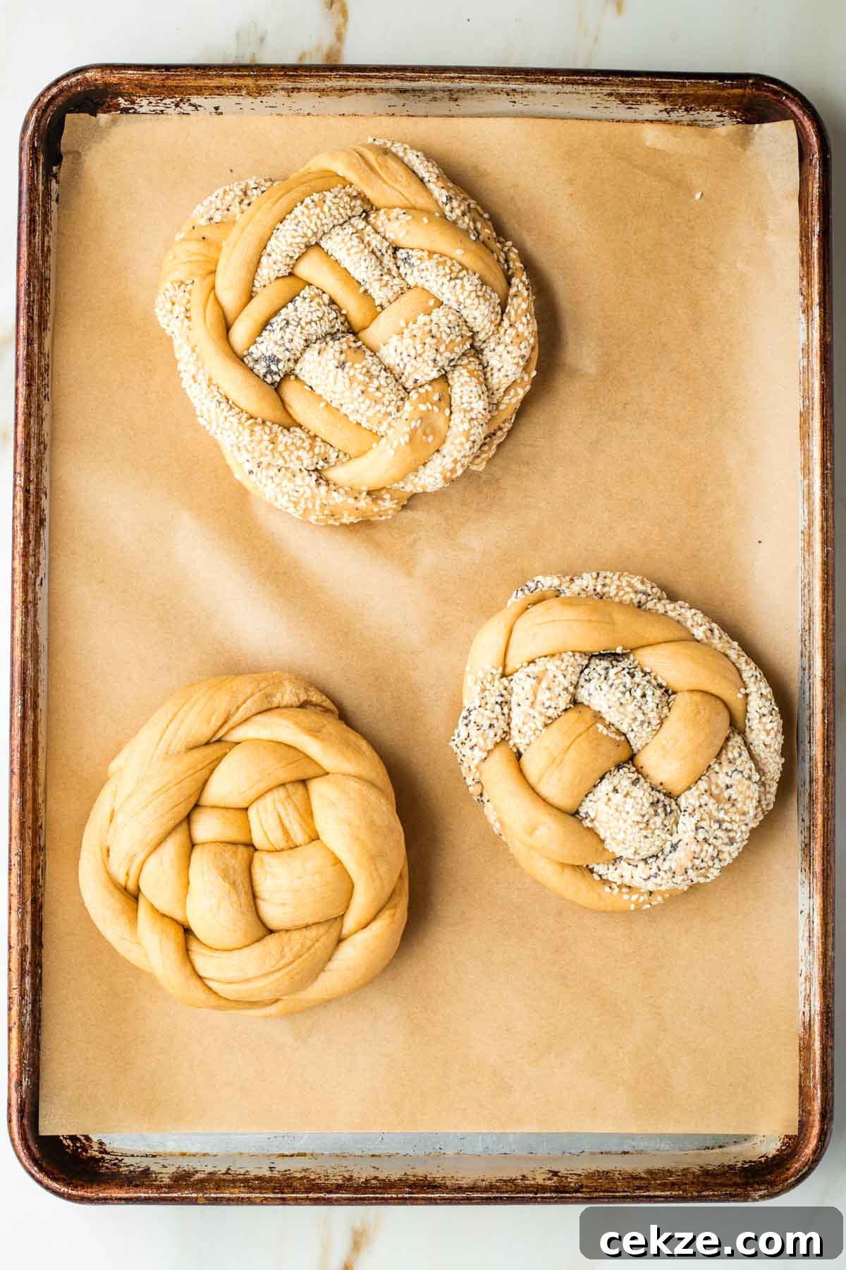 Sweet Round Challah Recipe: Soft, Shiny Braided Dinner Bread 31 Three round braided loaves of challah bread on a baking sheet. Some with poppy and sesame seeds.