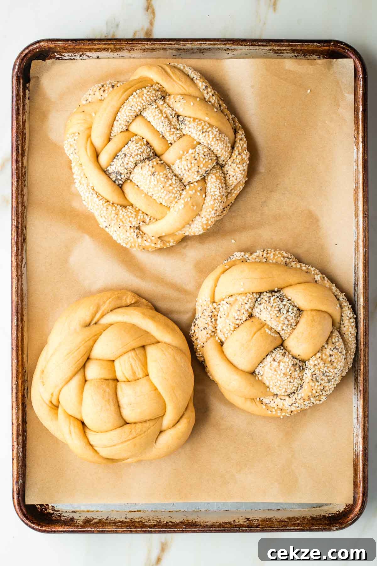 Sweet Round Challah Recipe: Soft, Shiny Braided Dinner Bread 32 Large, fluffy, round, braided loaves of unbaked challah bread on a parchment lined rimmed baking tray.